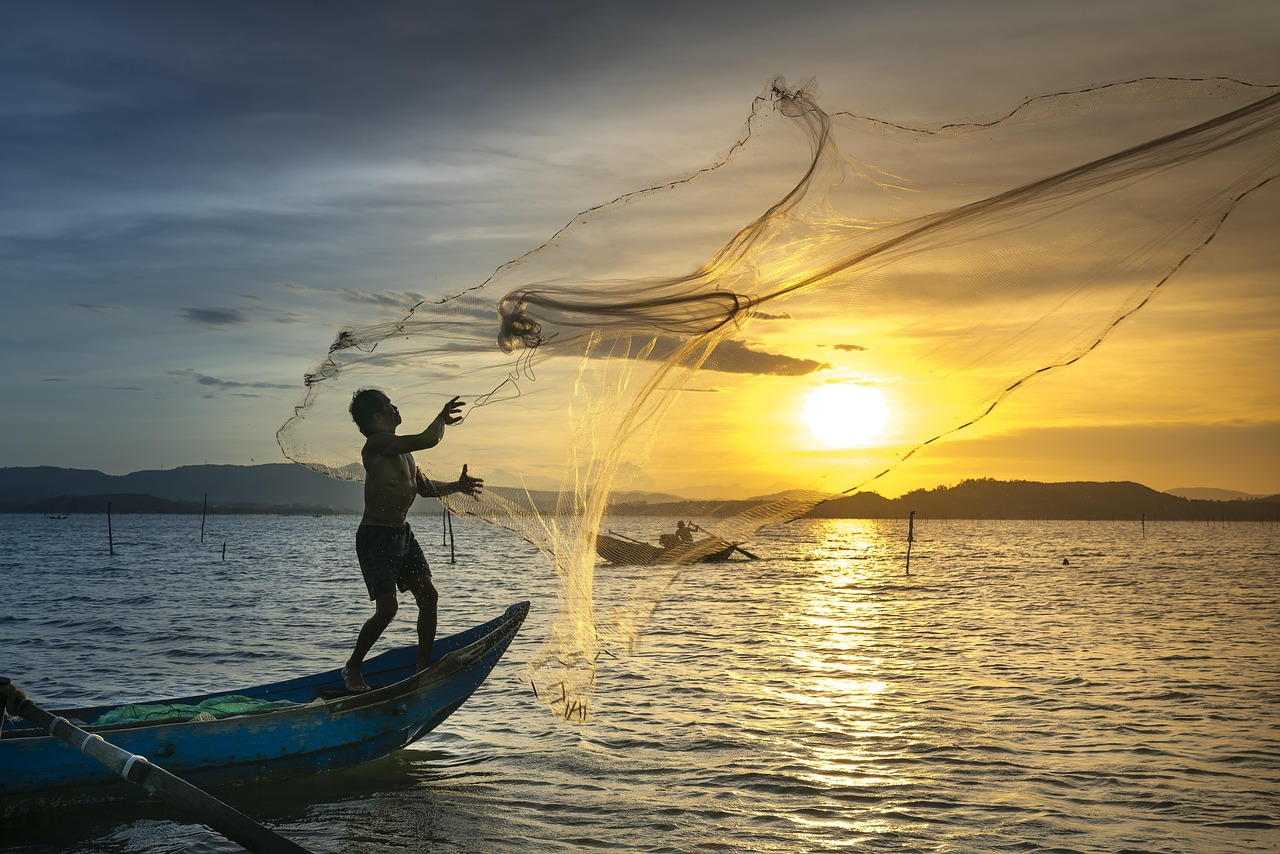 Fisherman casting a net from a boat at sunset