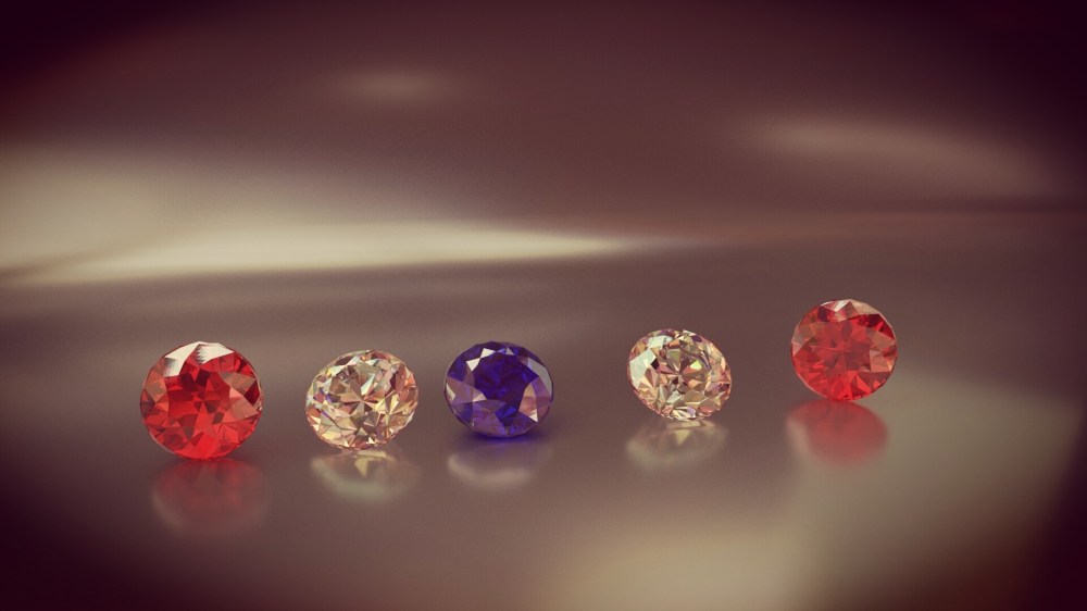 Five multicolored gemstones arranged in a row on a reflective surface.