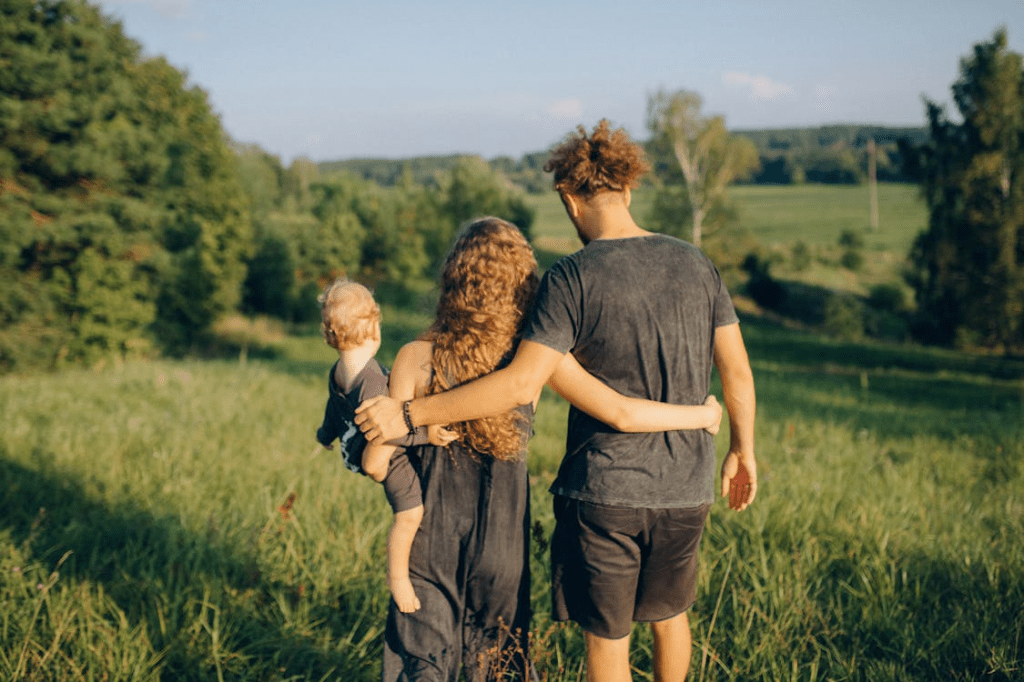 A couple walking together in a green field, with one partner holding a small child, showcasing a warm family moment.