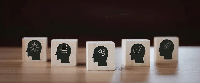Five wooden blocks featuring profiles of human heads with various icons symbolizing ideas, intelligence, skills, emotions, and tasks.