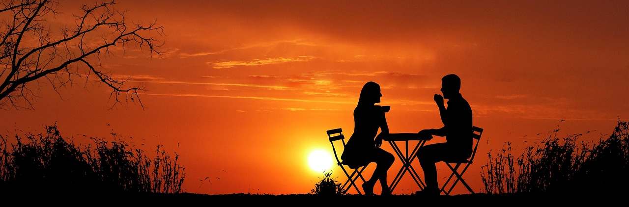 Romantic sunset outdoor dining scene Silhouettes of a man and woman in love sitting at a small table outdoors during sunset