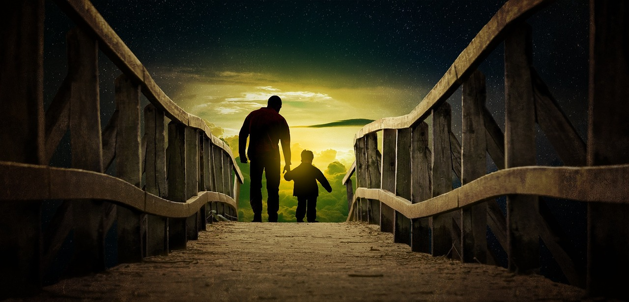Silhouetted figures walking on bridge at sunset A father and a son holding hands walking on a wooden bridge towards a glowing sunset sky