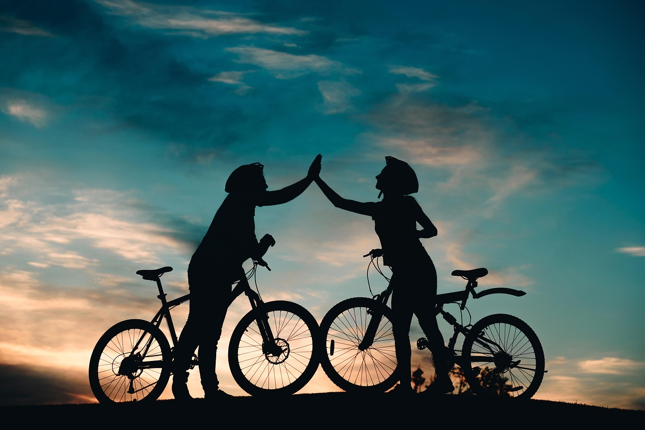 Two cyclists wearing helmets giving a high five at sunset