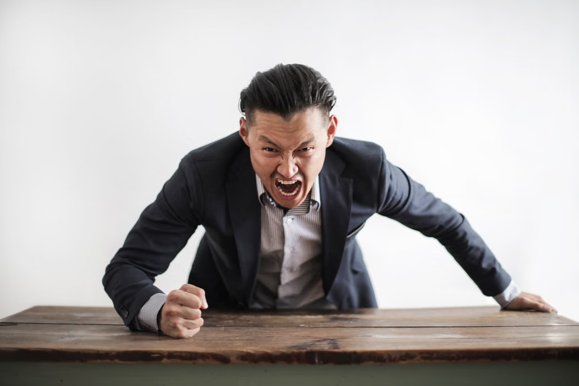 Angry man in suit leaning forward and pounding fist on table