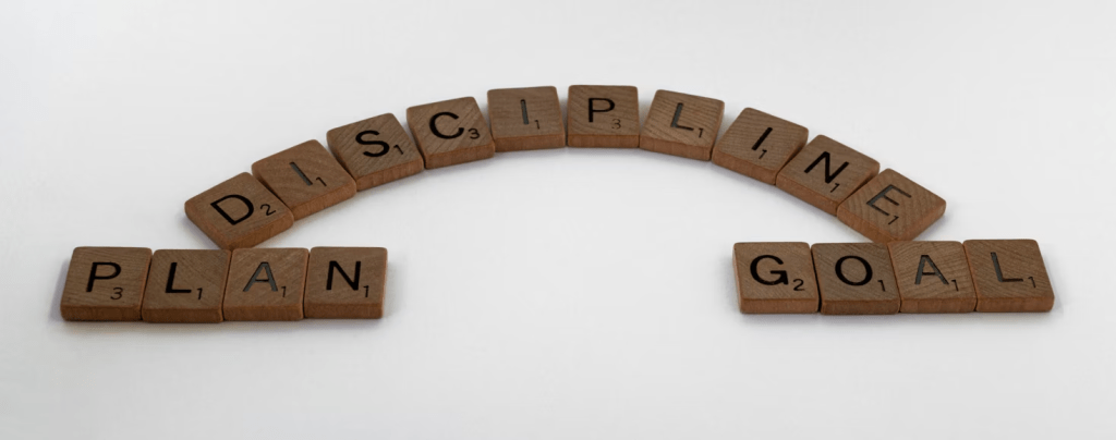 Wooden letter tiles arranged to spell 'DISCIPLINE', 'PLAN', and 'GOAL' on a white background.