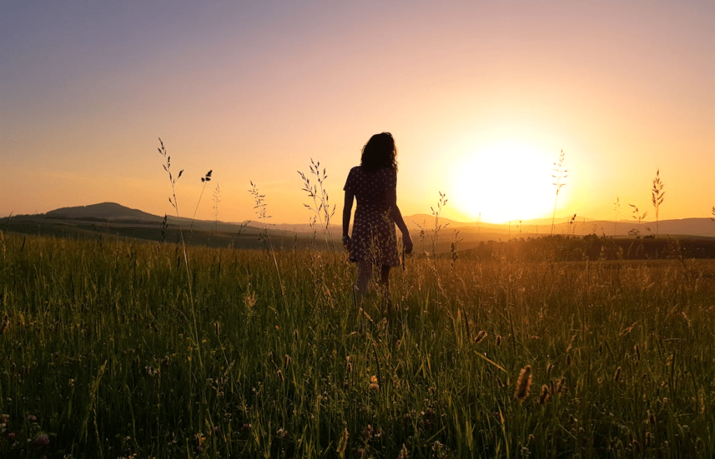 A silhouette of a woman walking through a field at sunset, symbolizing a journey of spiritual reflection and reconnection.