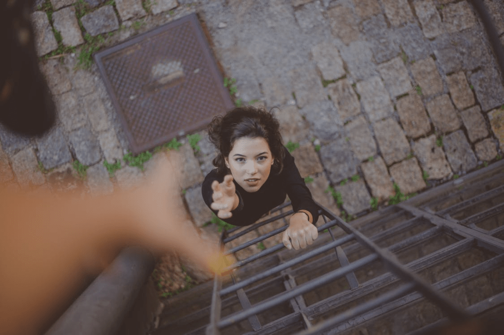 A young woman reaching up while climbing a ladder, looking upwards with determination.
