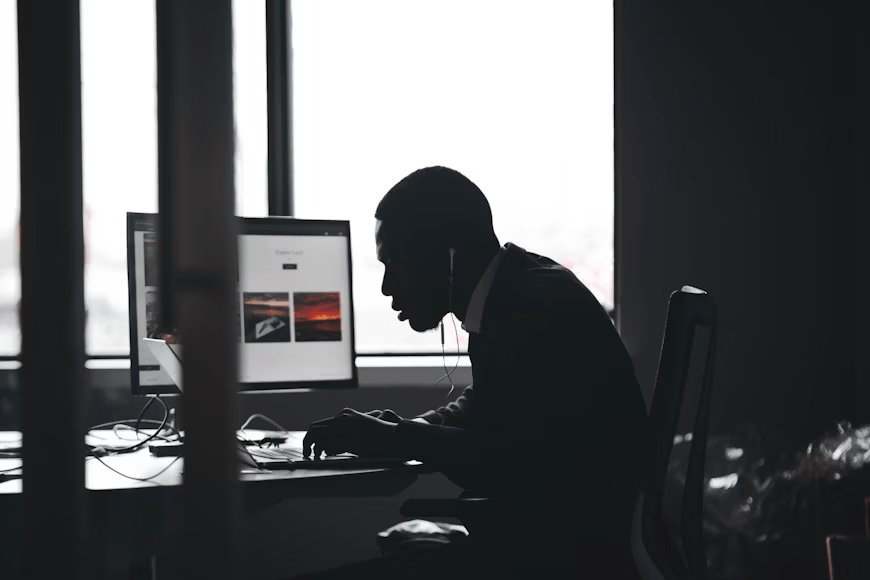 A silhouette of a person wearing headphones, focused on a computer screen in a dimly lit office, representing a moment of intense concentration or work.