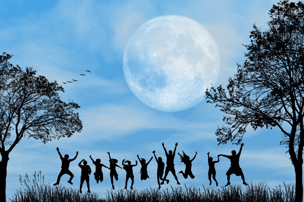 Silhouettes of people joyfully dancing and celebrating under a bright full moon with trees in the foreground, set against a blue sky.