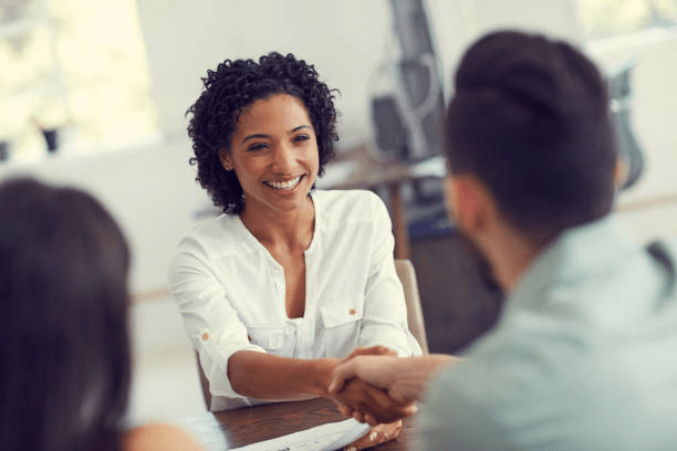 A smiling young woman in a white blouse shakes hands with a man, after earning her first employment