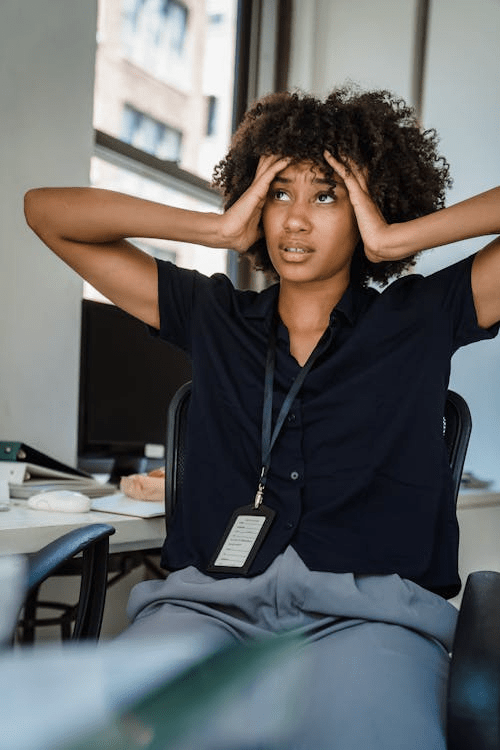 A stressed woman sitting at her desk in an office, holding her head in frustration while looking off into the distance.