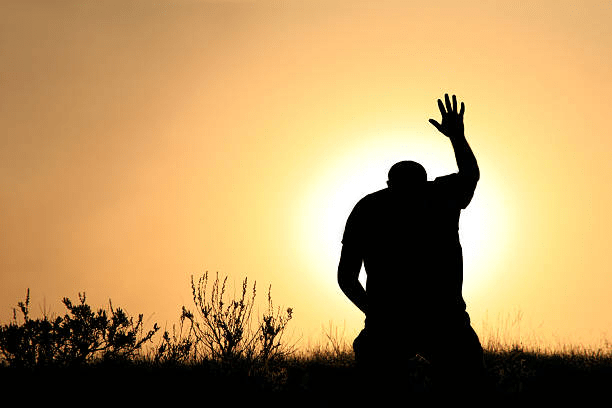 A silhouetted figure stands with one hand raised against a bright sunset, symbolizing prayer or worship.