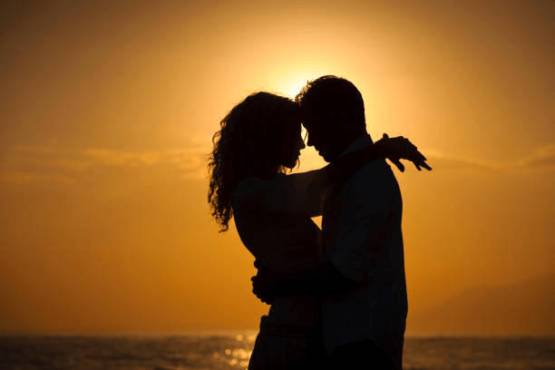 Silhouette of a couple embracing at sunset by the ocean, symbolizing love and connection.