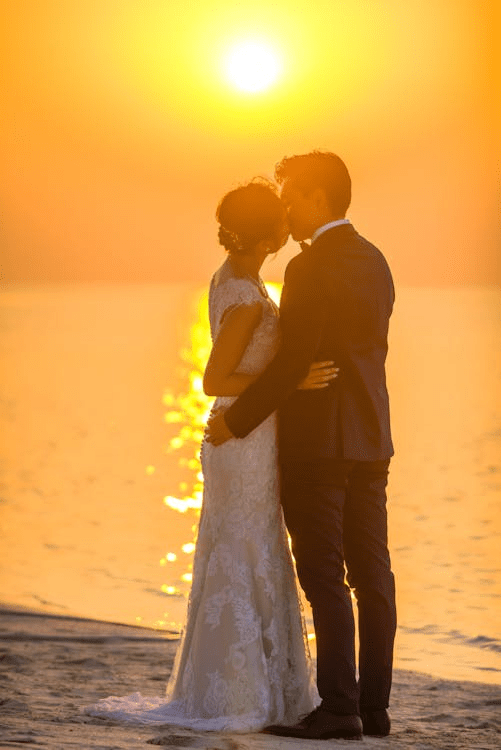 A couple embracing and sharing a kiss at sunset by the beach, symbolizing love and togetherness.