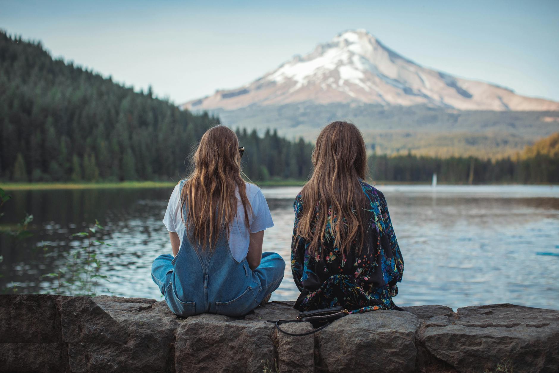 Two friends sitting on a rock by a lake, enjoying a scenic mountain view in the background.