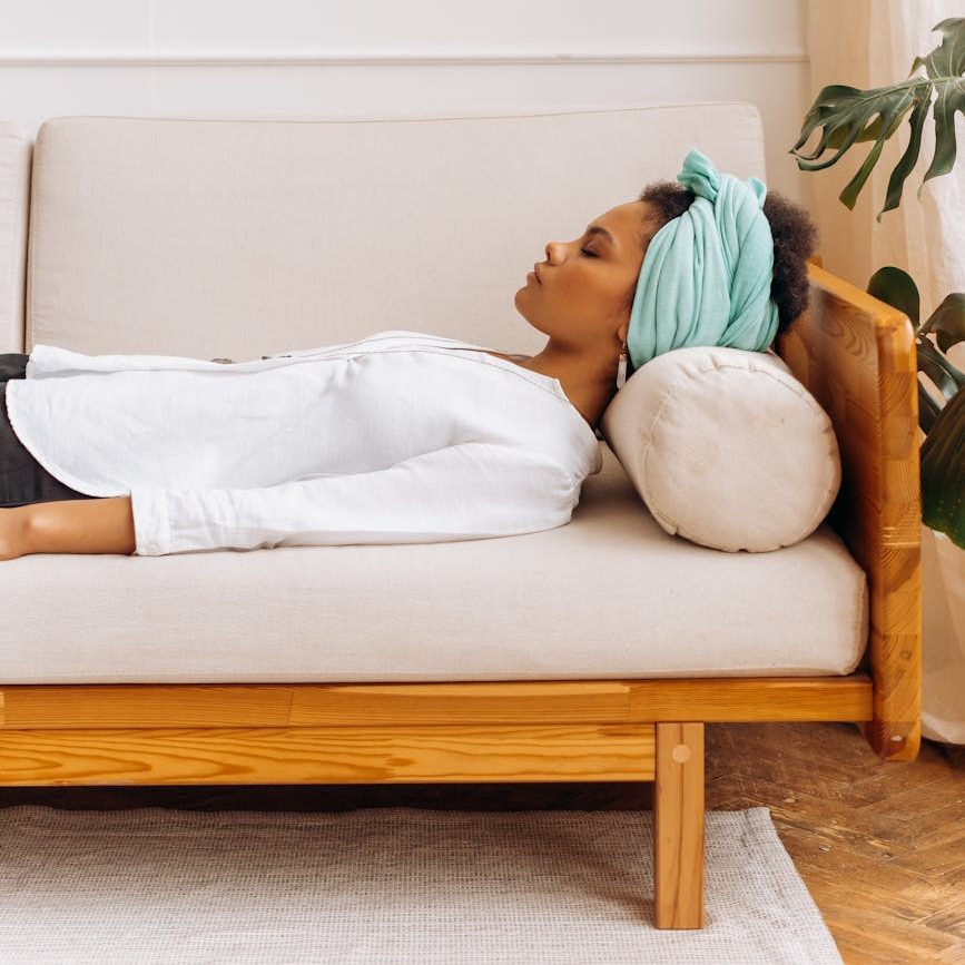 A woman lying on a couch with a turquoise headscarf and a relaxed expression, symbolizing peace and tranquility.