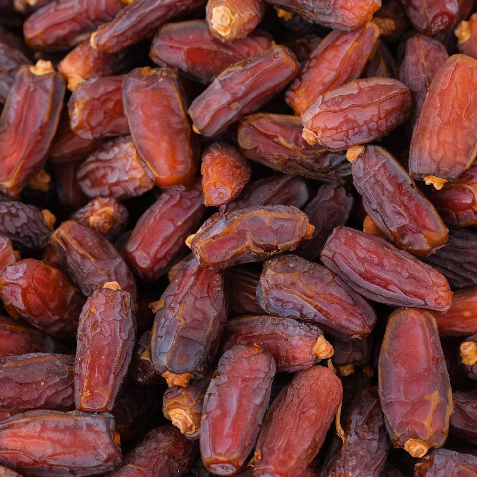 A close-up image of a pile of fresh, wrinkled dates showcasing their rich brown and reddish hues, highlighting their natural sweetness.