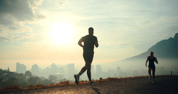 Two runners jogging on a path with a city skyline in the background, illuminated by a sunrise.