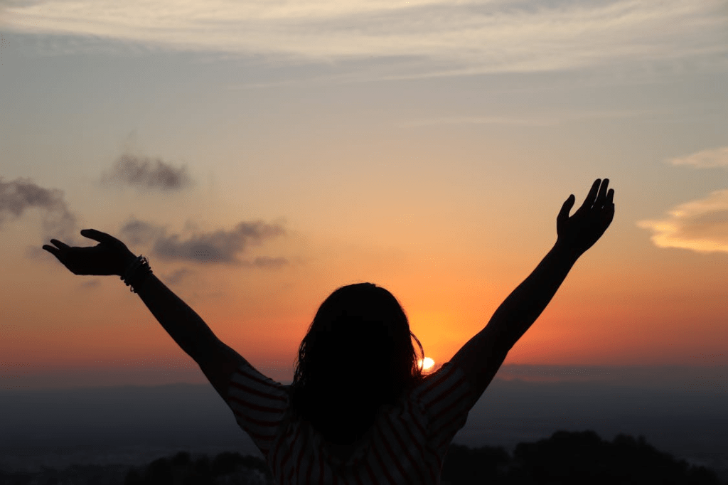 Silhouette of a person with outstretched arms against a vibrant sunset sky, symbolizing freedom and motivation.