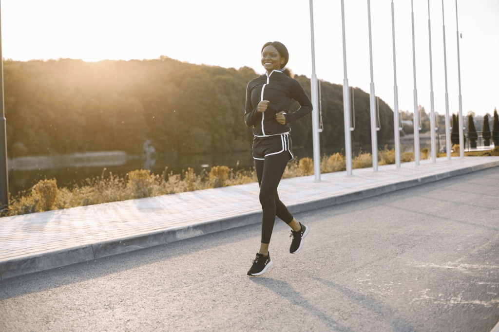 A person running along a pathway with trees in the background during sunrise or sunset, wearing athletic clothing.