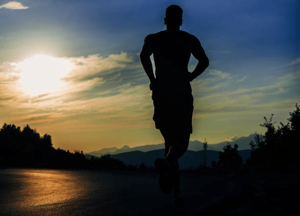 A silhouette of a runner jogging on a road during sunset, with mountains in the background.