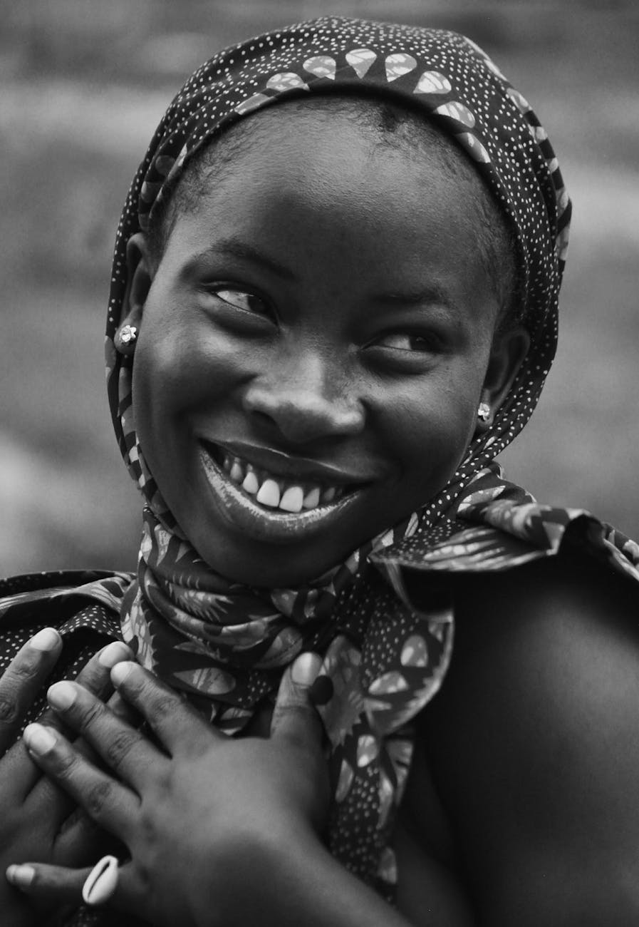 A smiling young woman in a patterned scarf, with her hands placed on her chest, conveying a sense of joy and warmth.