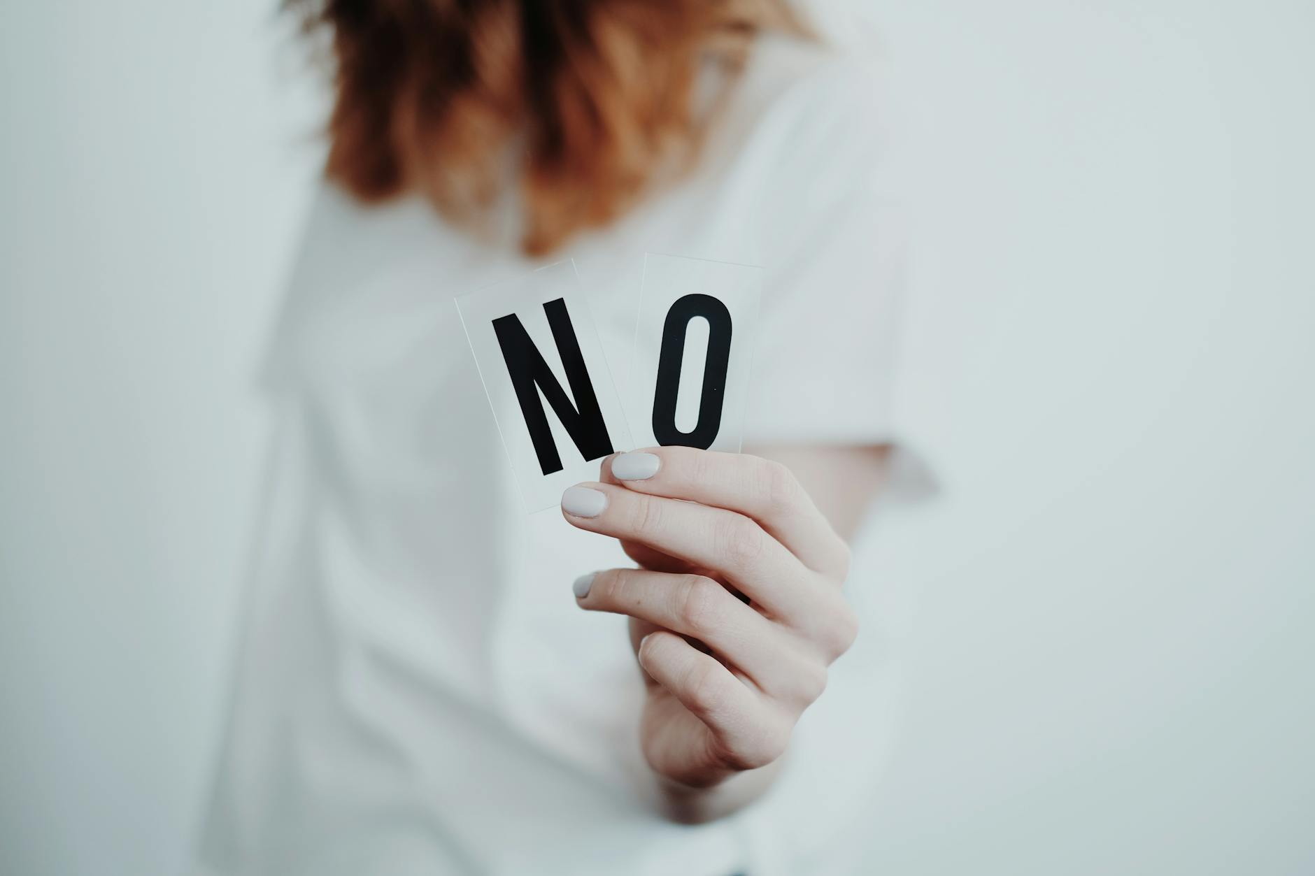 A person holding two cards displaying the word 'NO' with a neutral background, emphasizing the importance of setting boundaries.