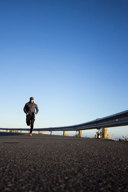 A person running on a deserted road with a guardrail, under a clear blue sky.