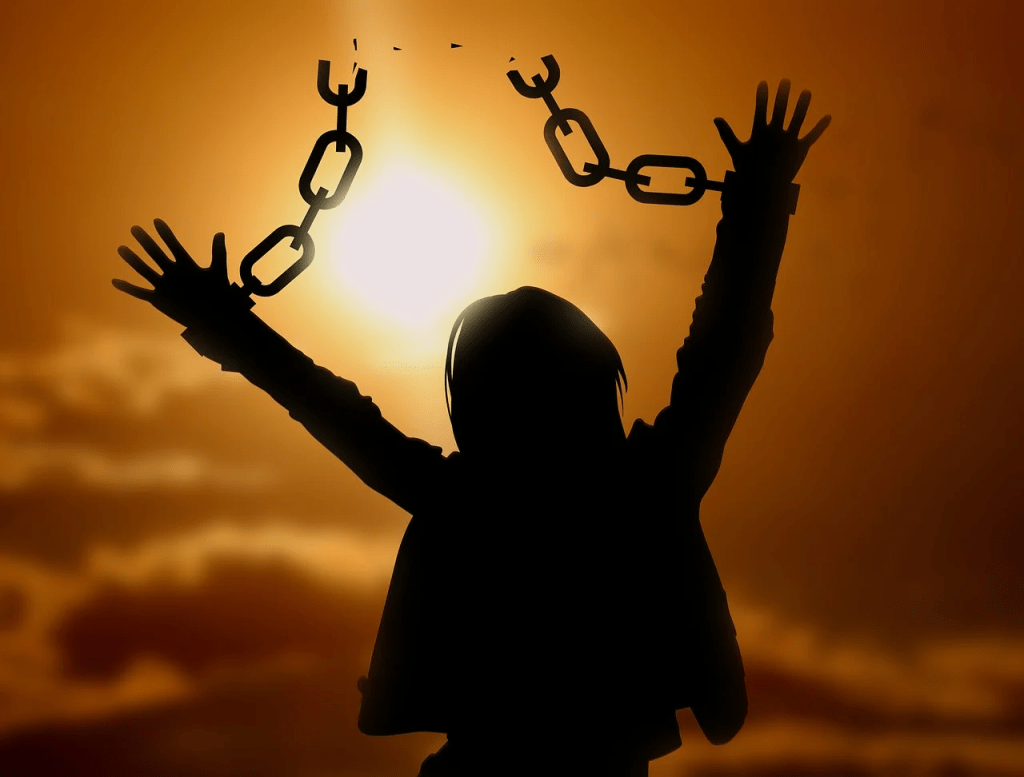 Silhouette of a person breaking free from chains against a sunset sky.