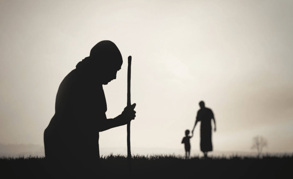 Silhouette of a woman with a walking stick, accompanied by a child holding hands with another figure in the background.