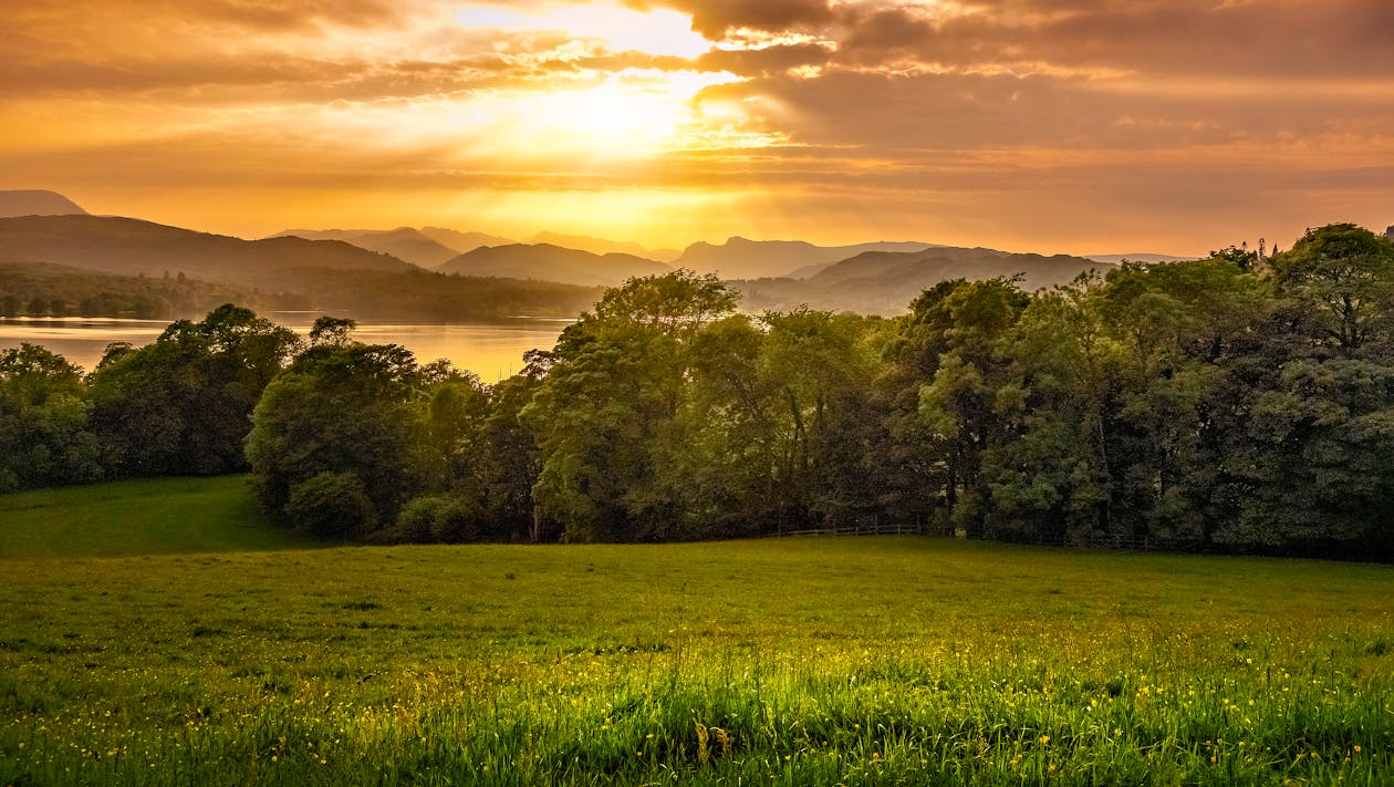 Sunset over lake and hills landscape Sunset over a lake with mountains in the background and green grassy field with trees in the foreground