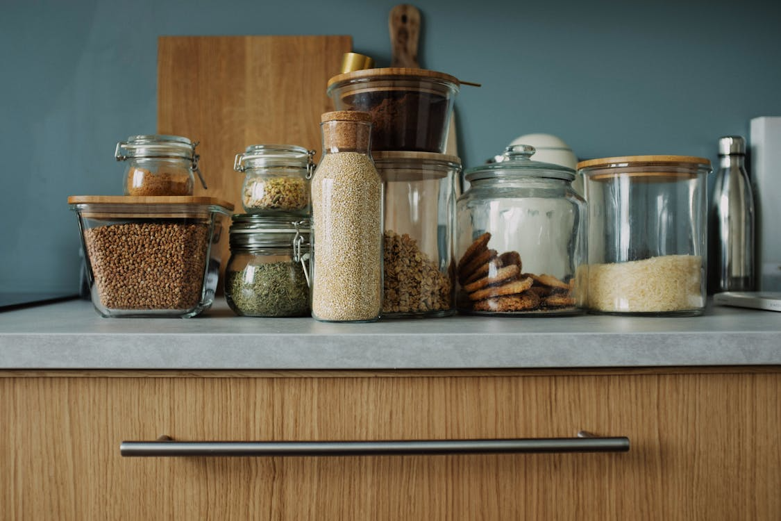 Various sealed glass jars containing dry food items like lentils, grains, cookies, and spices on a kitchen countertop