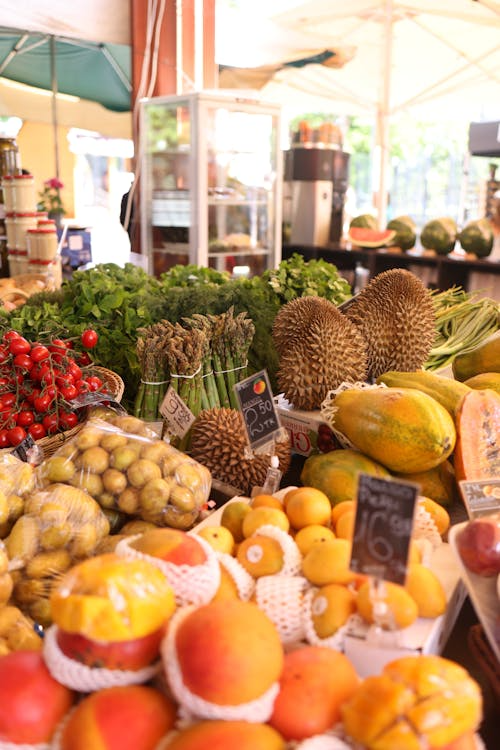Market stall with mangos, papayas, durians, and asparagus. Tags show 'Mango 50 TR' and '16.90'.