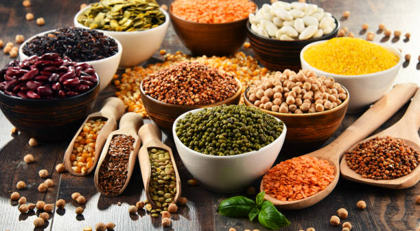 An assortment of legumes, grains, and seeds in various bowls and wooden spoons.