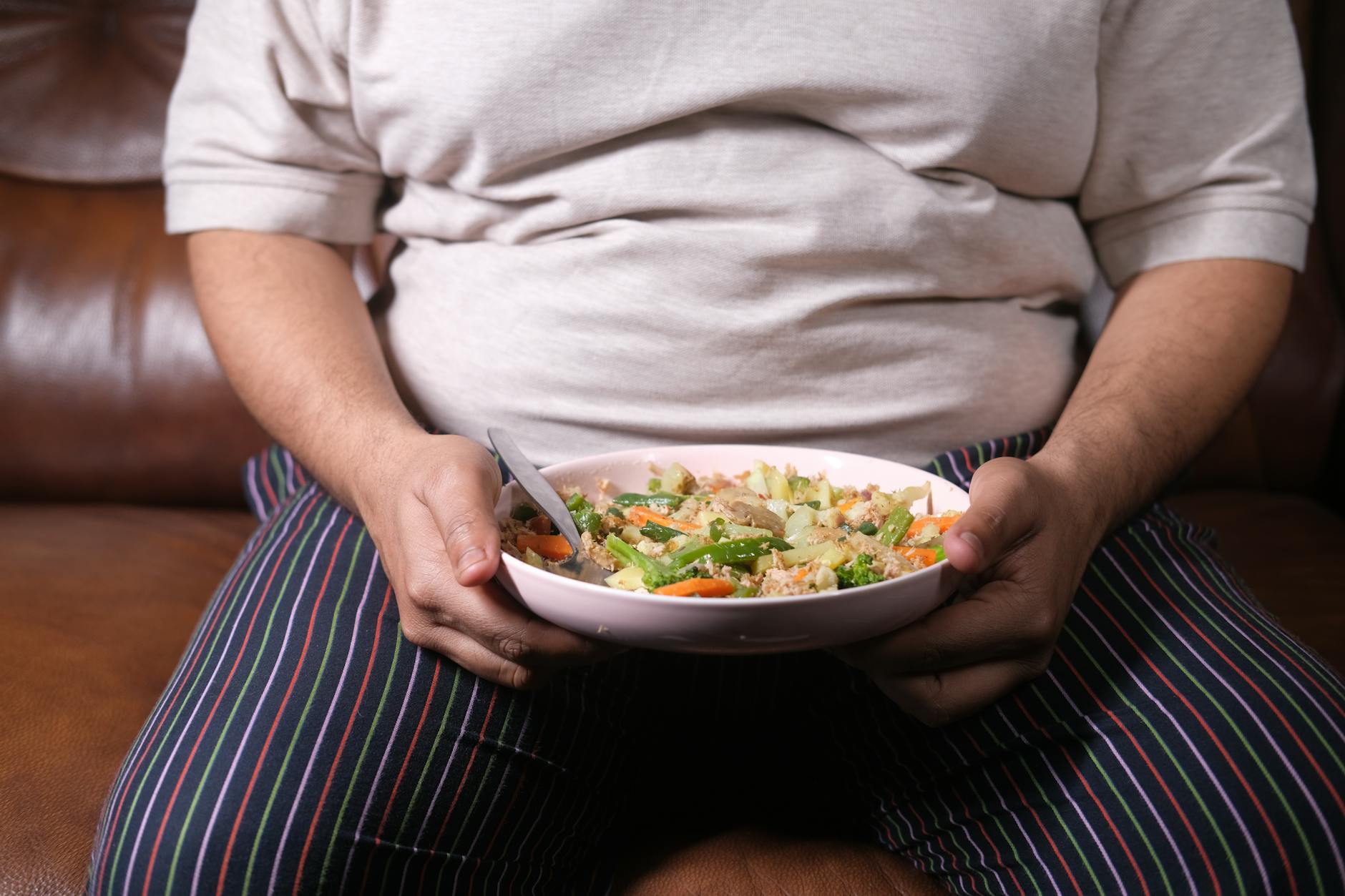 Person holding a bowl of mixed vegetable stir-fry with a spoon