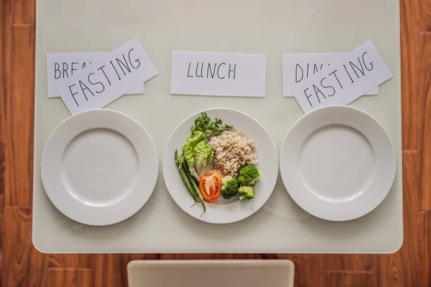 Three plates on a table labeled as fasting for breakfast and dinner, and lunch with vegetables and rice