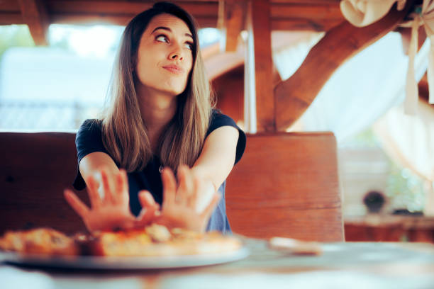 A woman refusing to eat food placed before her on on a table in a cozy wooden room with natural light