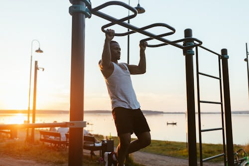 Outdoor fitness at sunset by lake Man exercising on monkey bars outdoors at sunset beside a lake