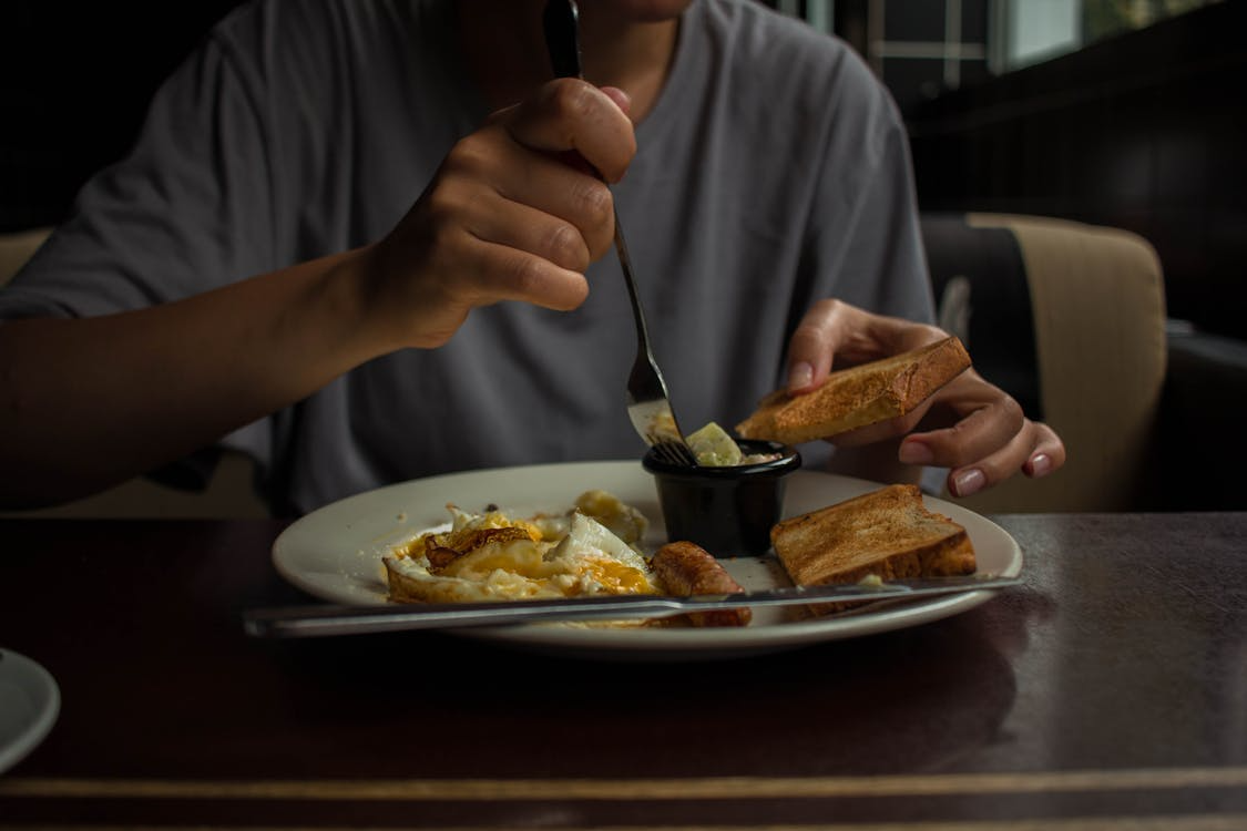 Person dipping butter onto toast with cooked eggs and sausage on plate