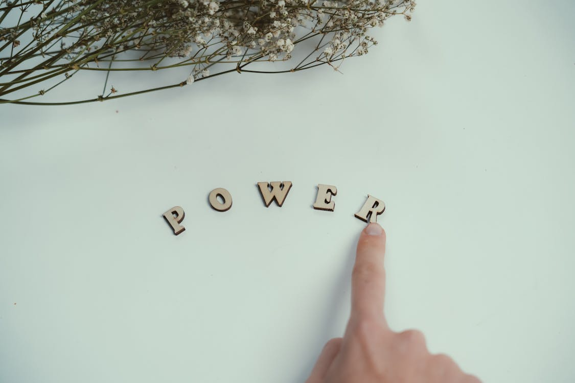 Conceptual empowerment with wooden letters Finger touching wooden letter R in the word POWER arranged on white surface