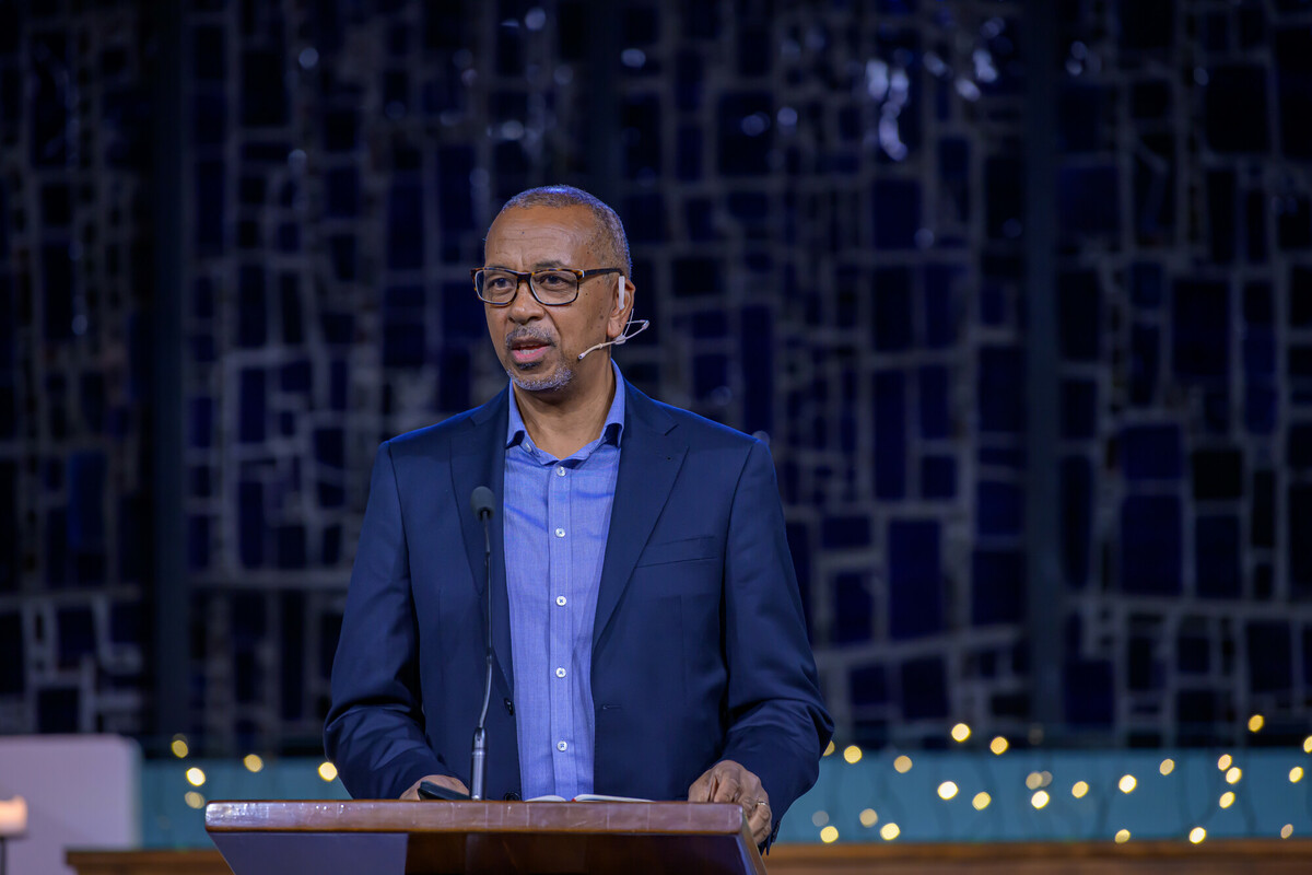 Speaker delivering presentation at conference Man wearing glasses and a blue suit speaking at a podium with microphone in front of a stained glass background