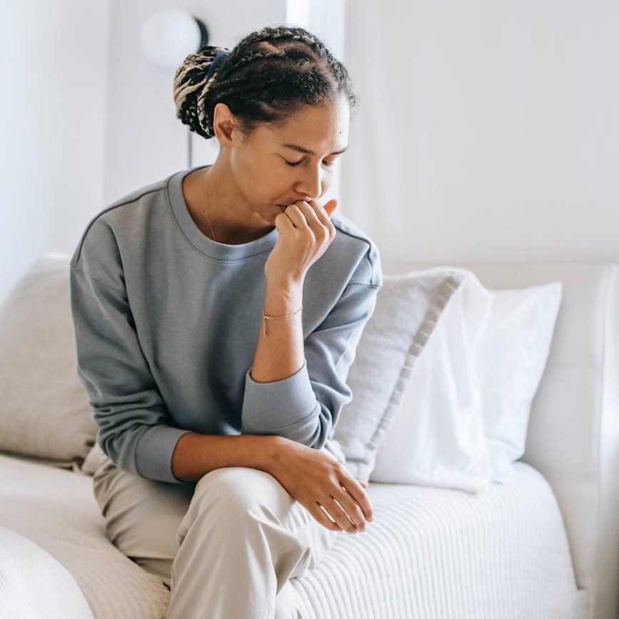A person sitting on a bed, resting their chin on their hand, looking thoughtful or concerned