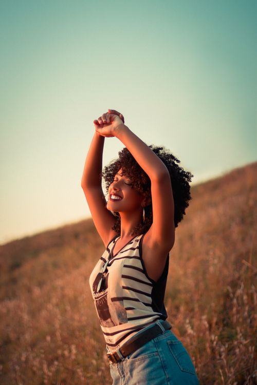A person standing in a field with arms raised, eyes closed, smiling and enjoying the sunlight