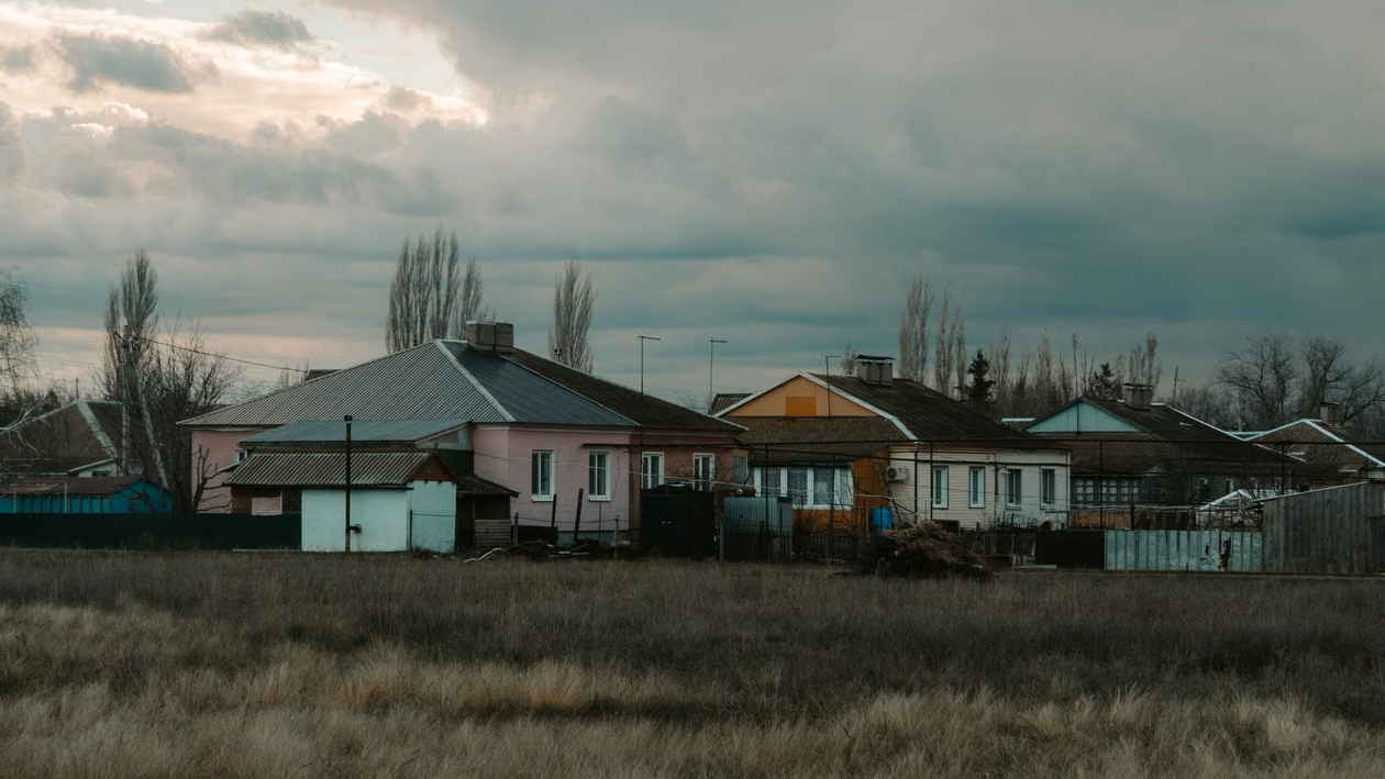 Rural houses at dusk with overcast sky Row of rural houses with fenced yards under dark, cloudy sky at dusk
