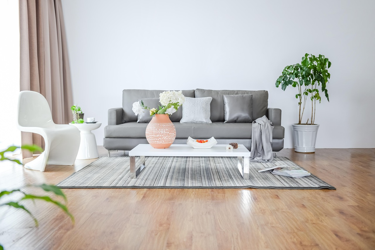 Modern minimalist living room setup Gray sofa with cushions, white coffee table with vase and bowl, white chair, indoor plants