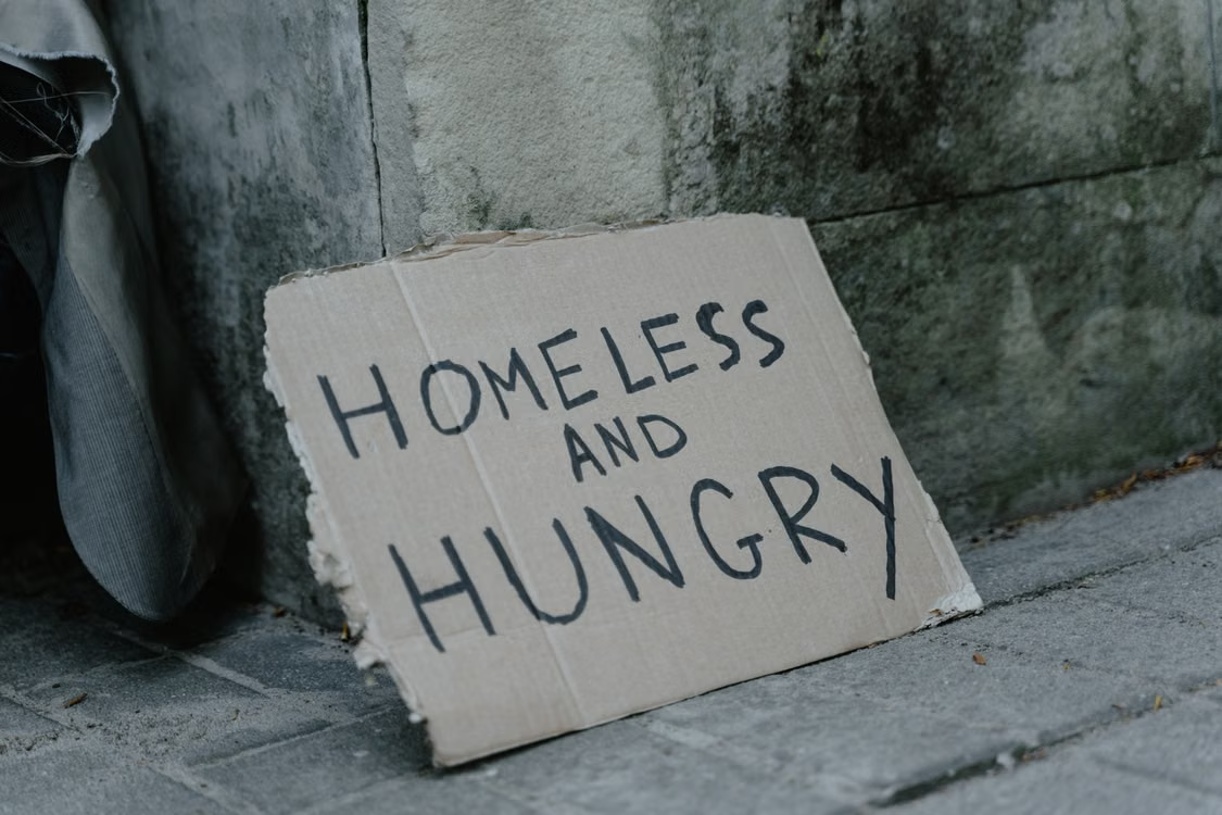 Raising awareness of homelessness and hunger Cardboard sign reading "HOMELESS AND HUNGRY" beside a sidewalk and wall