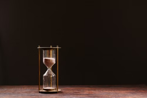 Traditional hourglass symbolizing time and patience Glass hourglass with sand on a wooden table against a dark background