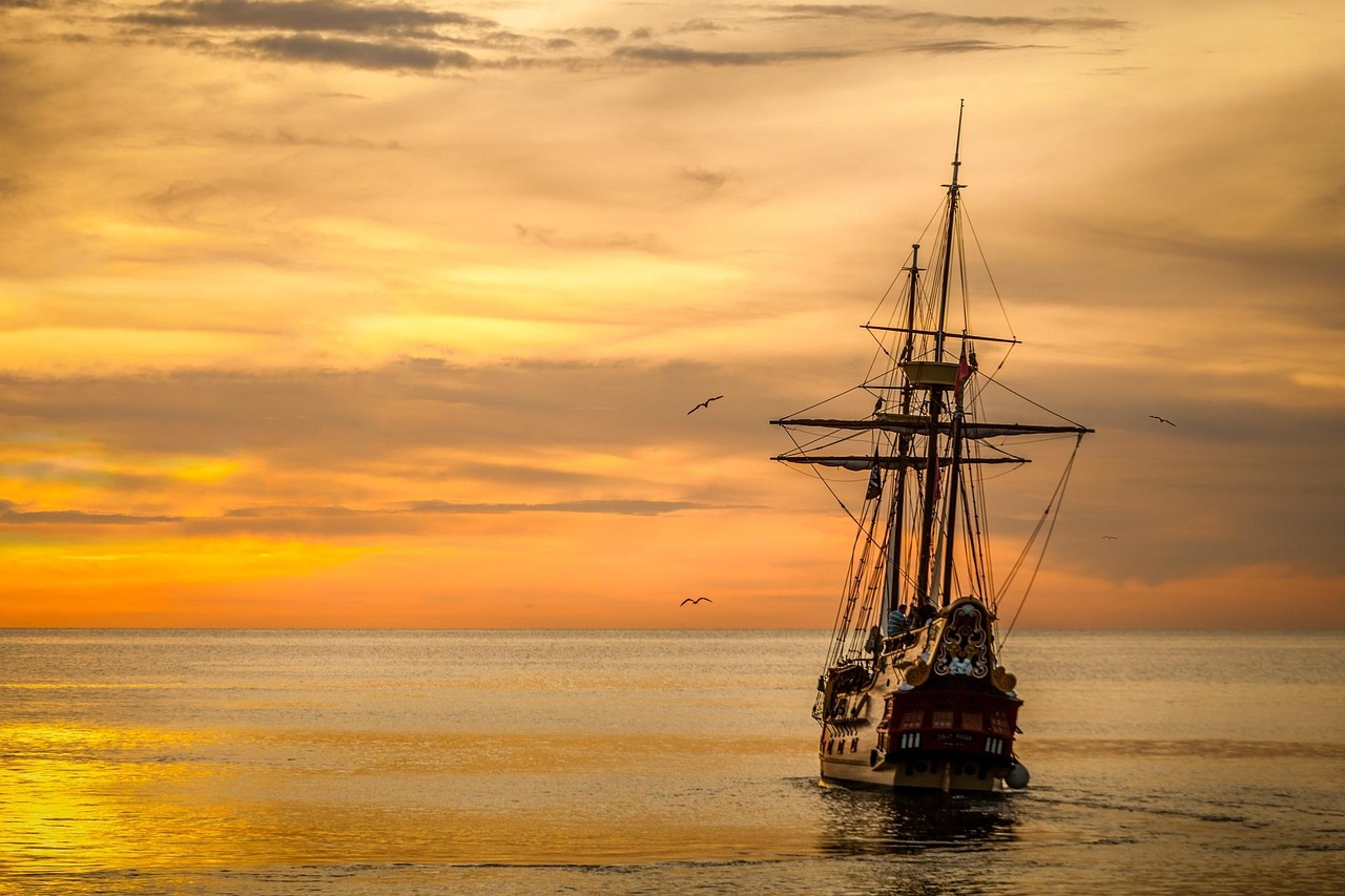 Historic sailing ship at golden sunset Sailing ship approaching across calm water at golden sunset