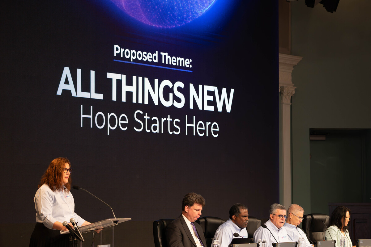 Speaker at a panel beneath text reading “Proposed Theme: ALL THINGS NEW Hope Starts Here”