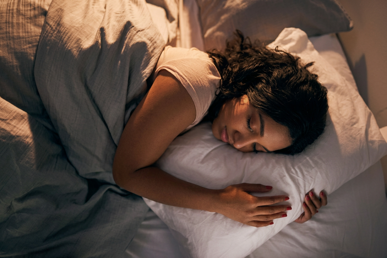 Person sleeping on their side while hugging a white pillow under a gray blanket